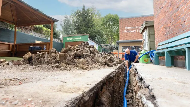 An Aspect tradesperson laying new water supply pipes in a trench dug in a school playground.