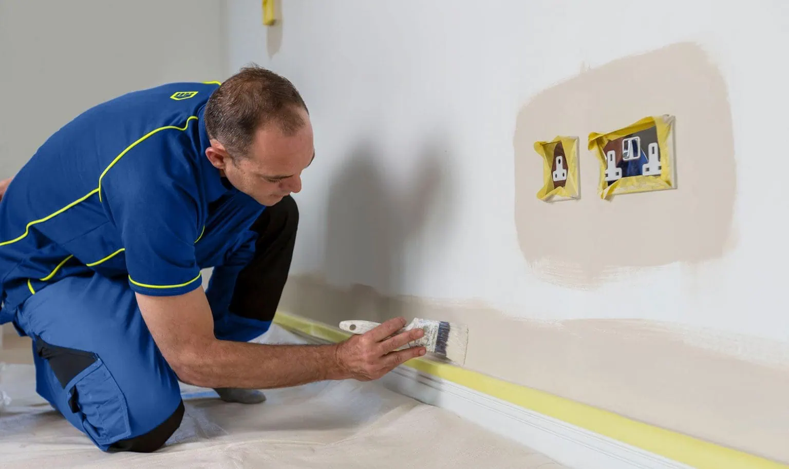 An Aspect painter decorator cutting in with coloured emulsion around electrical sockets and along skirting board.