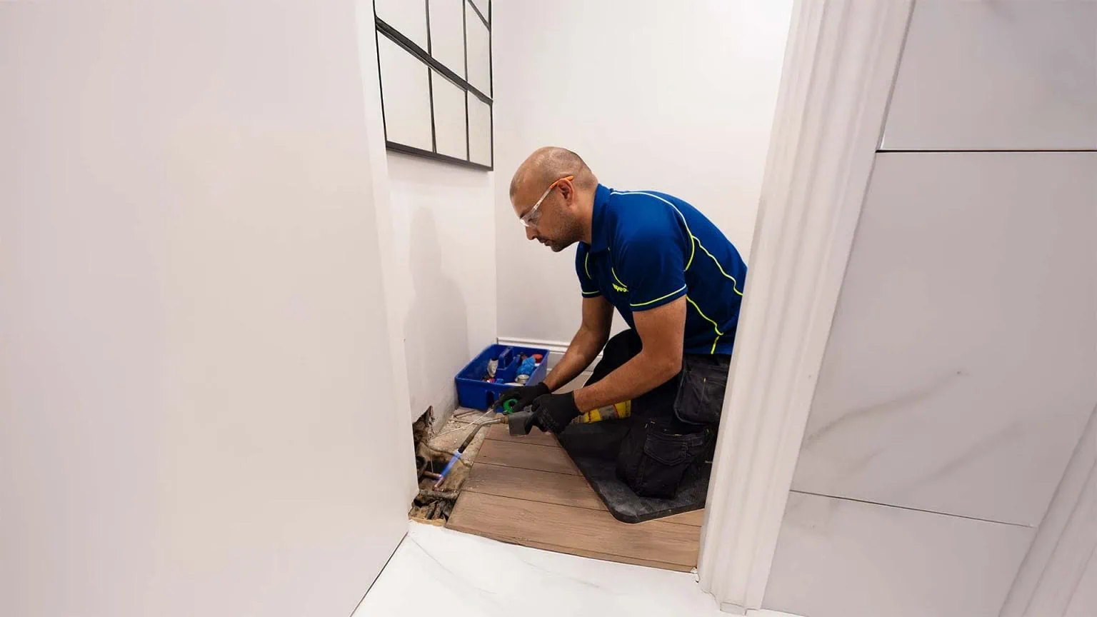 An Aspect plumber uses a gas torch to repair a leak in a copper pipe exposed beneath a bathroom floor.