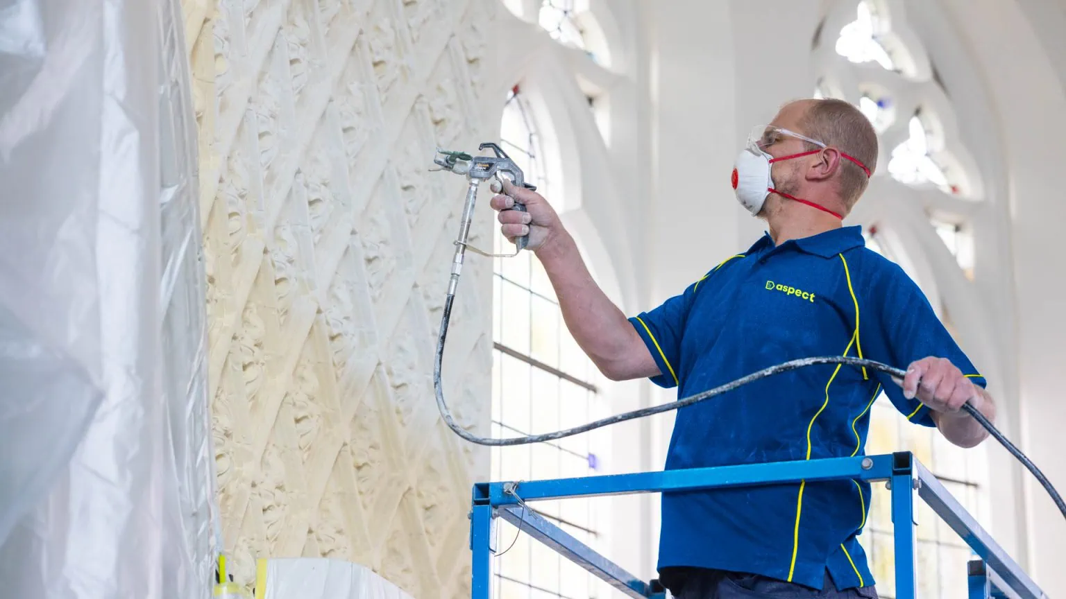 An Aspect painter decorator on a lift platform painting the interior of a religious building.